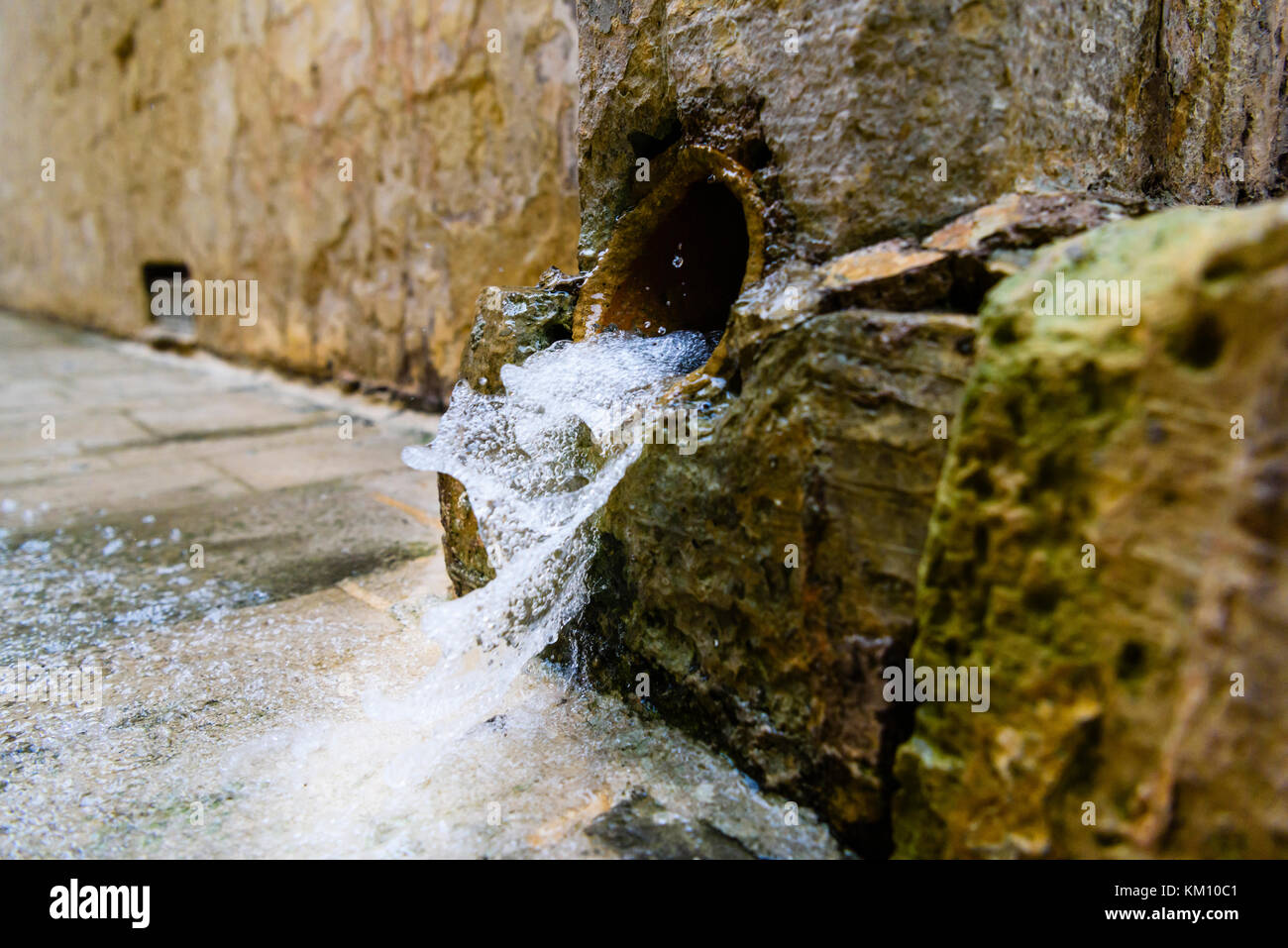 Rainwater gushing from a very old downspout onto a footpath Stock Photo