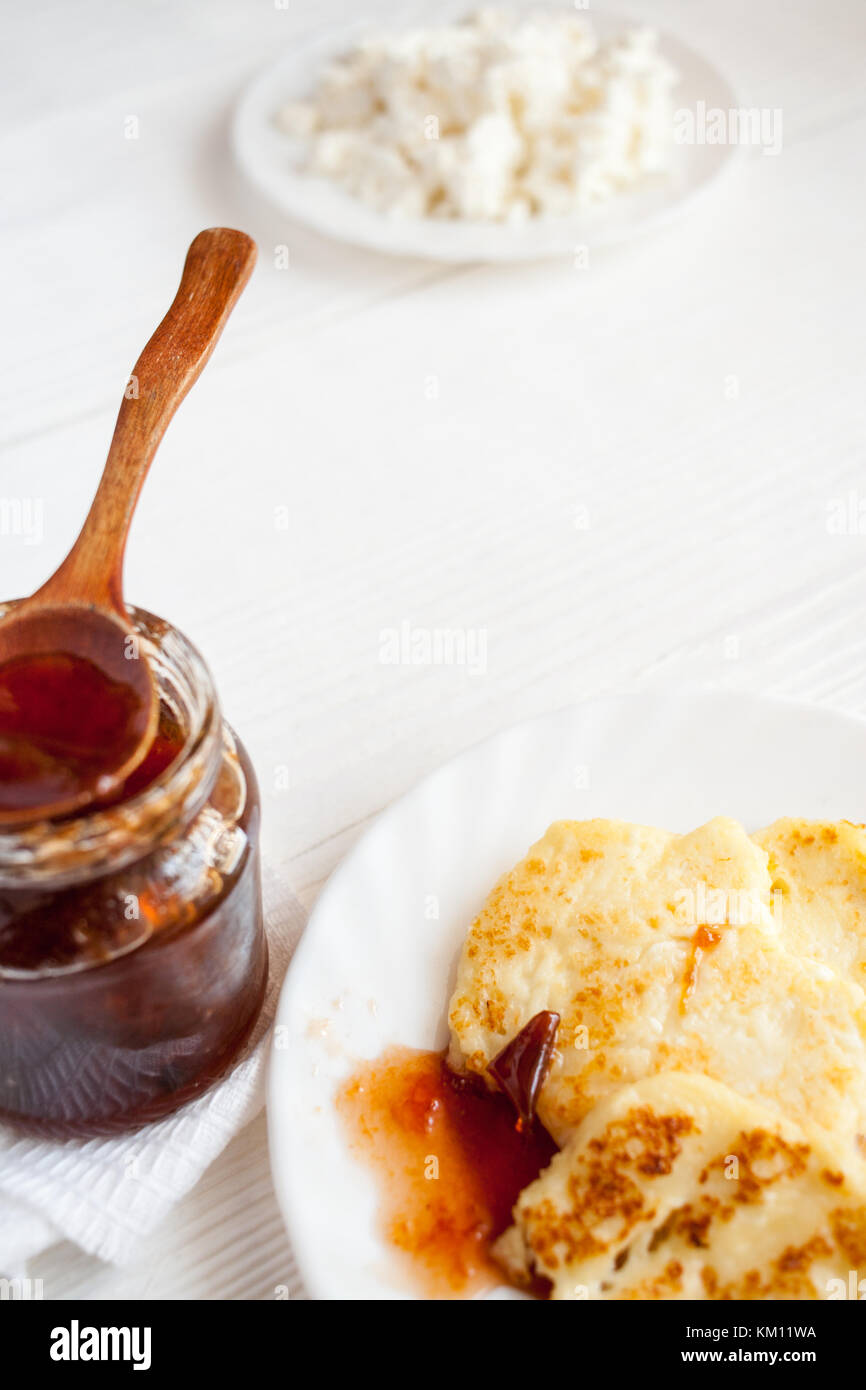 Curd pancakes, plum jam in glass jar and fresh curd on wooden table. Selective focus. Diagonal composition. Stock Photo