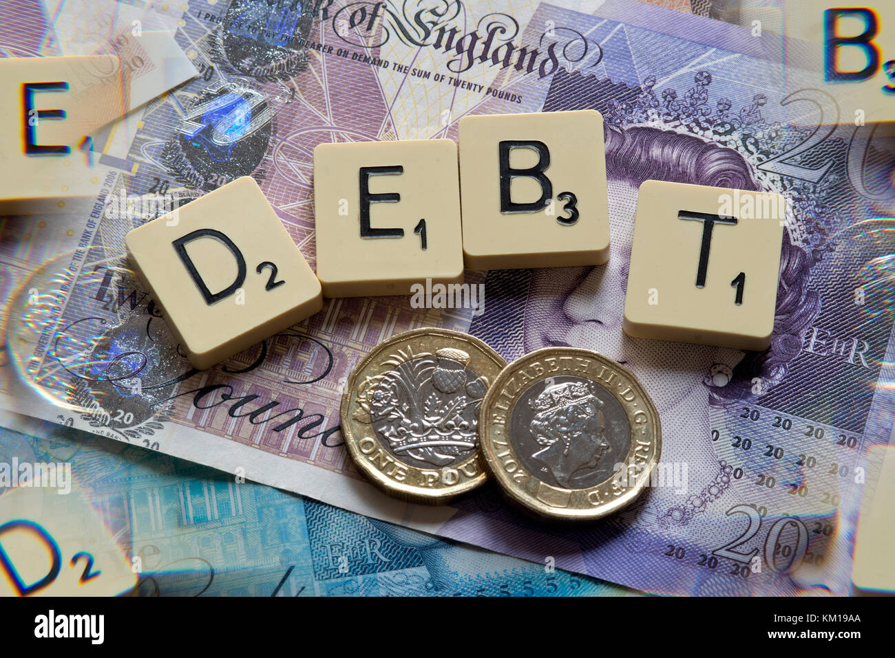 Scrabble letters spelling DEBT with new British pounds (GBP) £20, £10, £5 notes and new British pound coins. Stock Photo