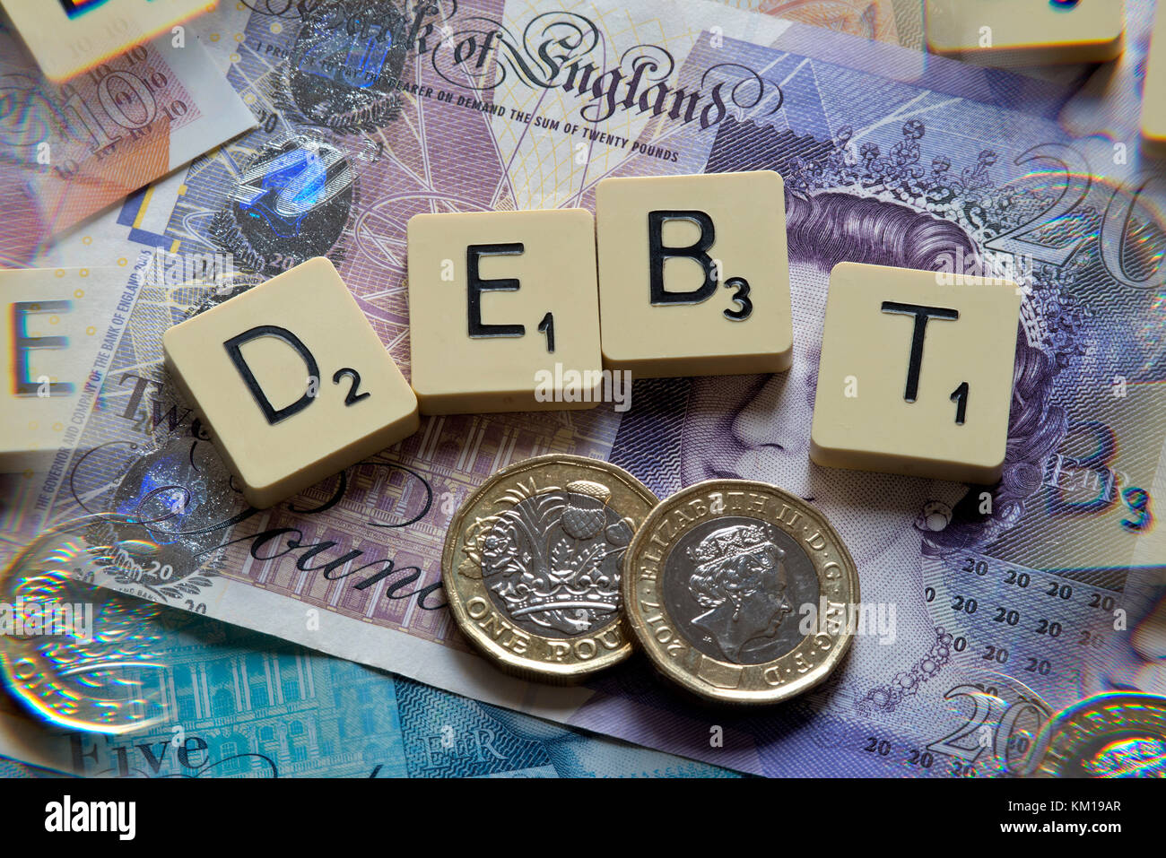 Scrabble letters spelling DEBT with new British pounds (GBP) £20, £10, £5 notes and new British pound coins. Stock Photo