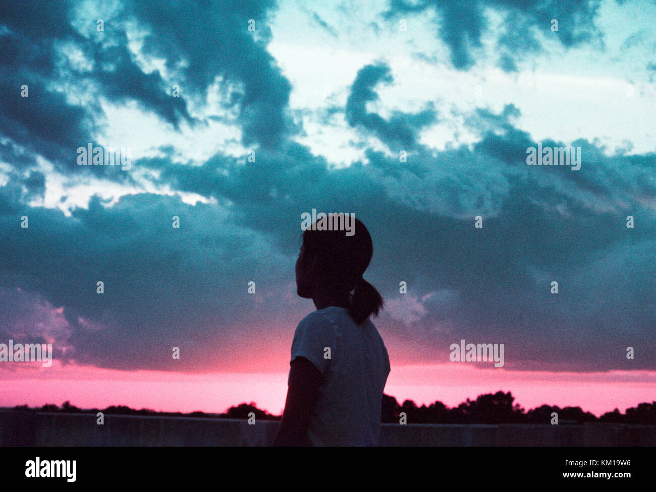 Silhouette of woman looking out at the cloudy sunset sky Stock Photo