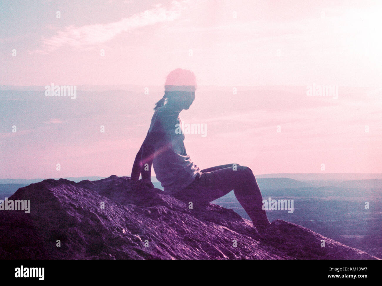 Double Exposure of woman on rock looking out at landscape at sunrise Stock Photo