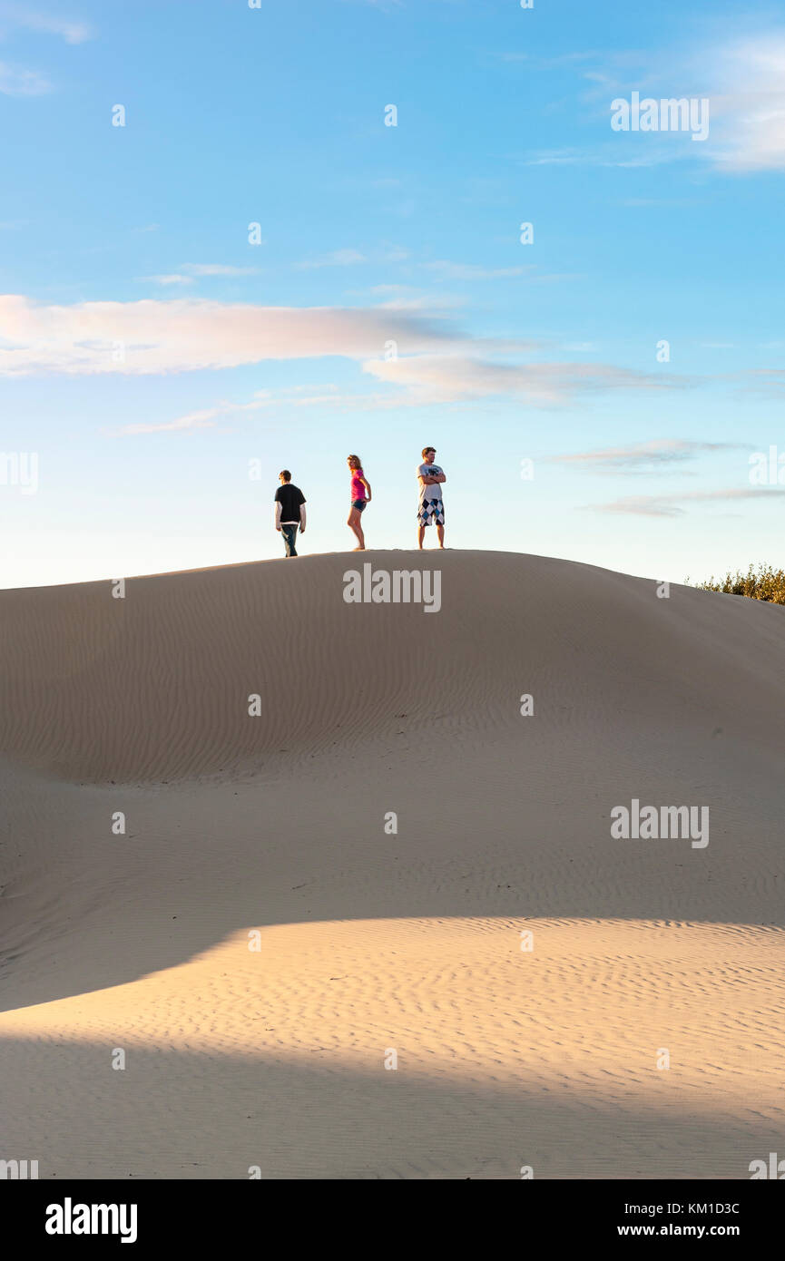 Three teens walking on the edge of sand dunes at Oceano Dunes State Vehicular Recreation Area, Oceano Dunes Natural Preserve, California, USA. Stock Photo