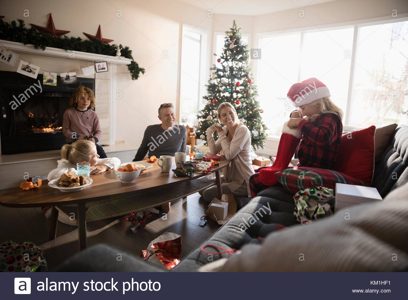 Curious girl opening Christmas stocking with family in living room ...