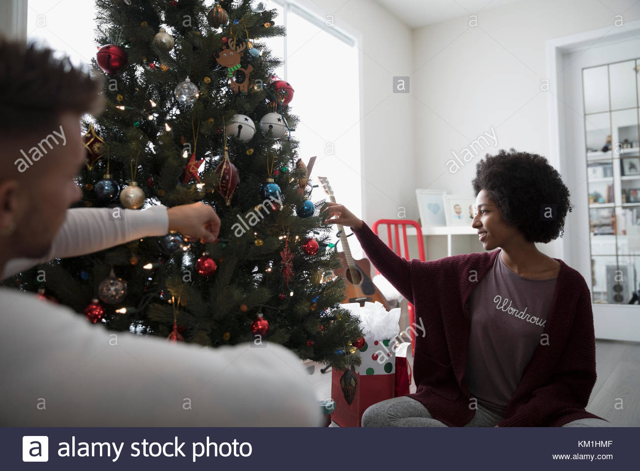 Young couple in pajamas decorating, hanging ornaments on Christmas tree in living room Stock Photo
