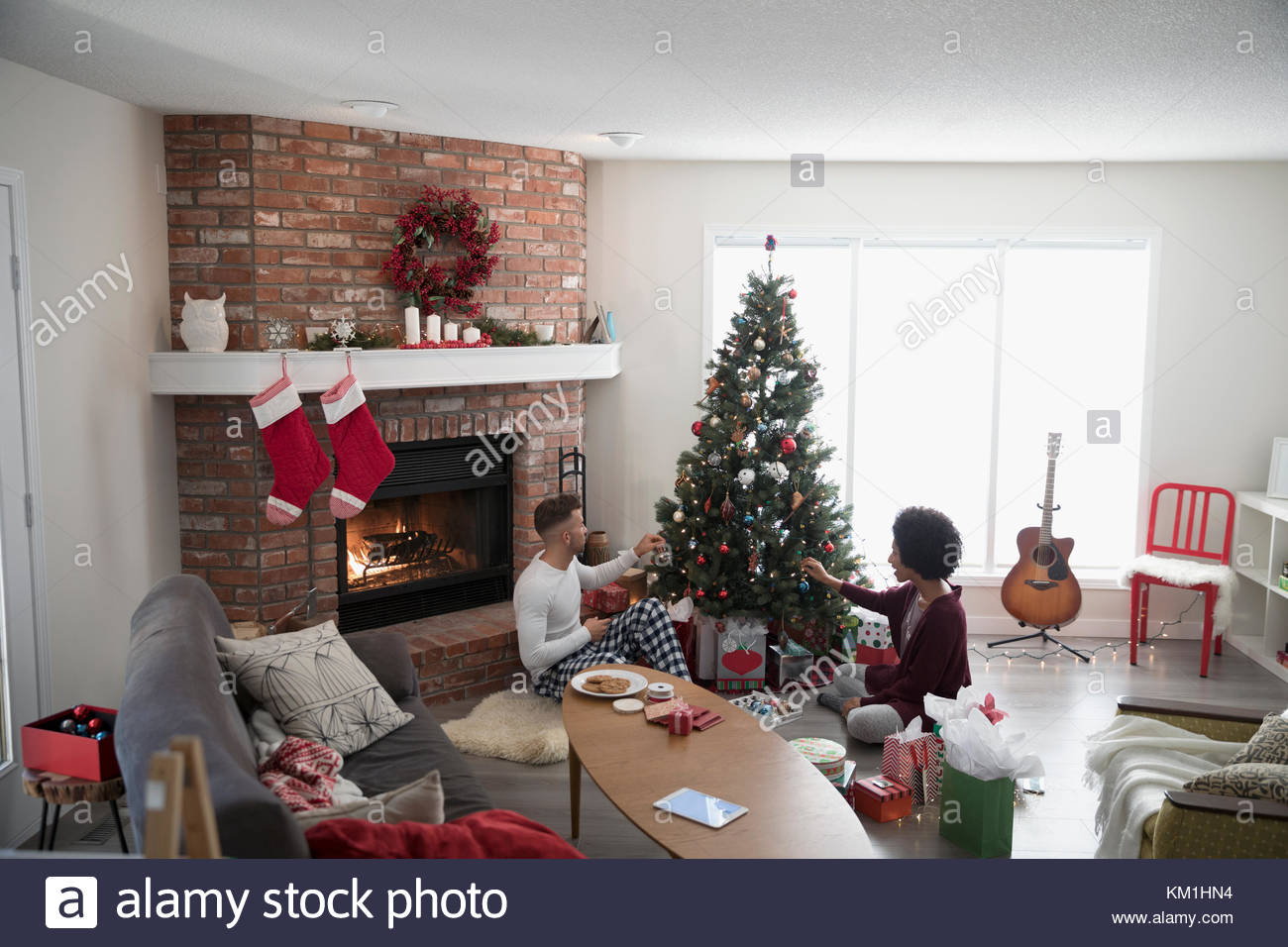 Young couple in pajamas decorating, hanging ornaments on Christmas tree in living room Stock Photo