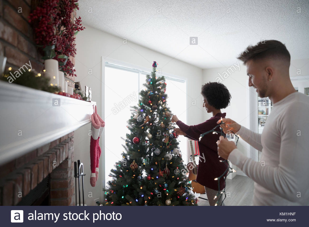 Young Couple Decorating Hanging Christmas Lights On Tree In