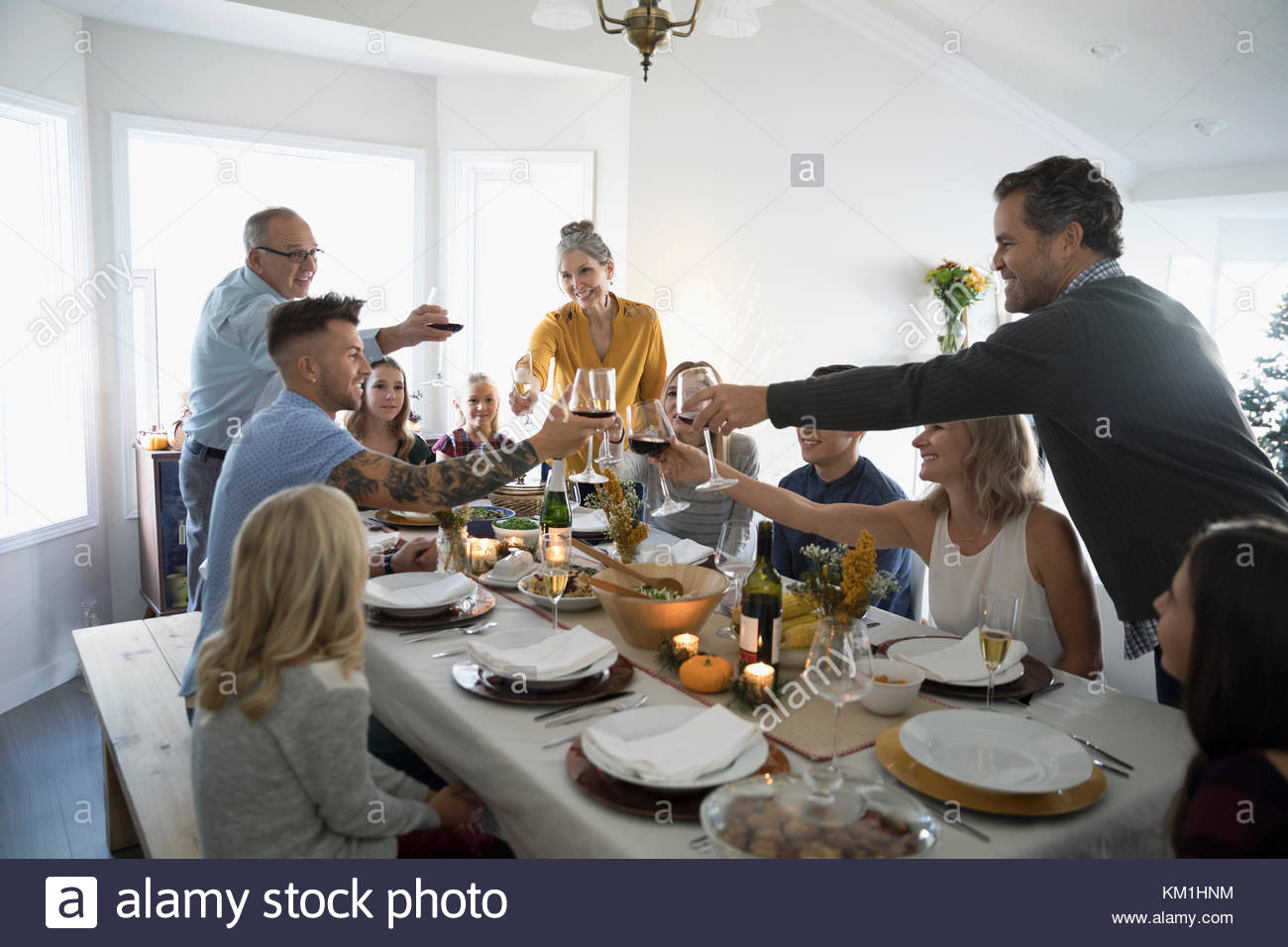 Family and friends toasting champagne and wine glasses at Thanksgiving dinner table Stock Photo