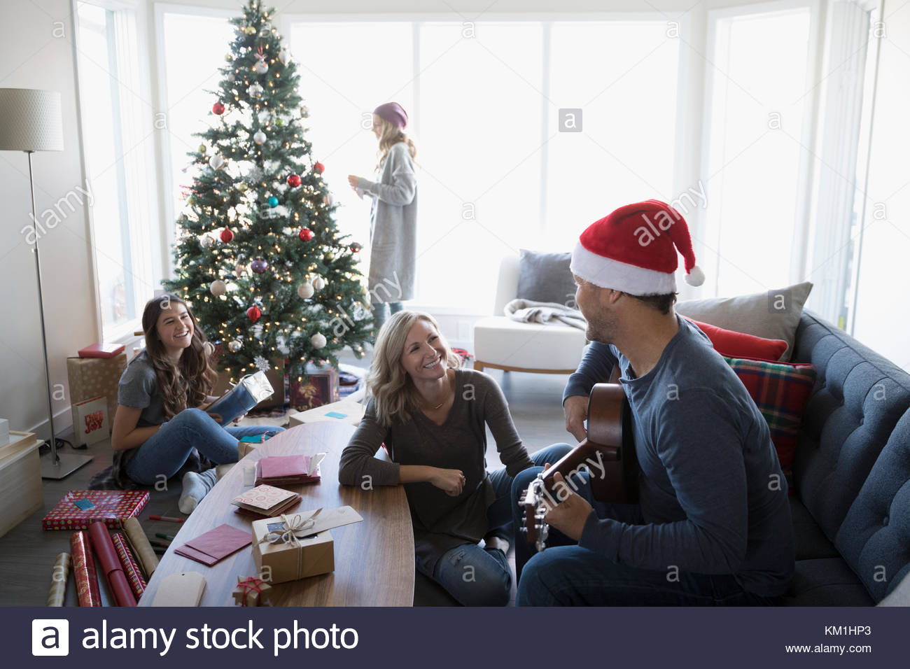 Family playing guitar and wrapping gifts, decorating Christmas tree in living room Stock Photo