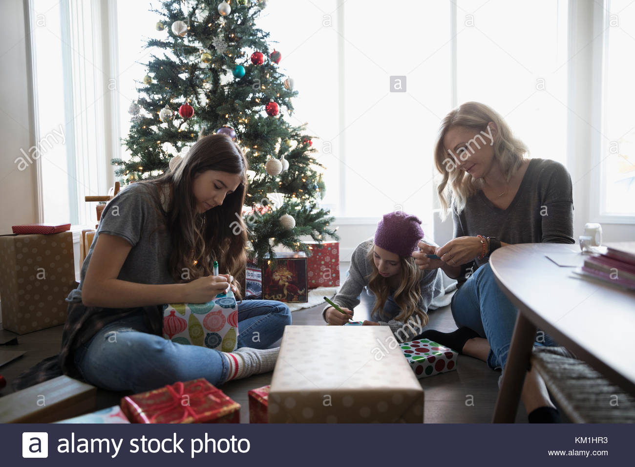 Mother and daughters wrapping Christmas gifts near Christmas tree in