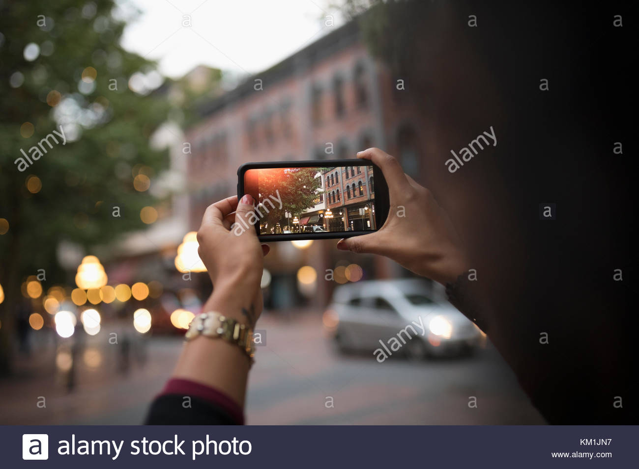Over the shoulder view woman using camera phone, photographing urban night street Stock Photo