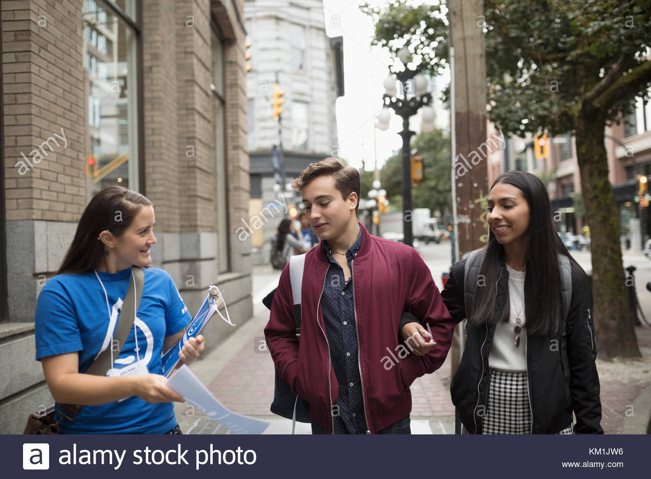 Political young woman canvassing on urban sidewalk, showing petition to young couple Stock Photo