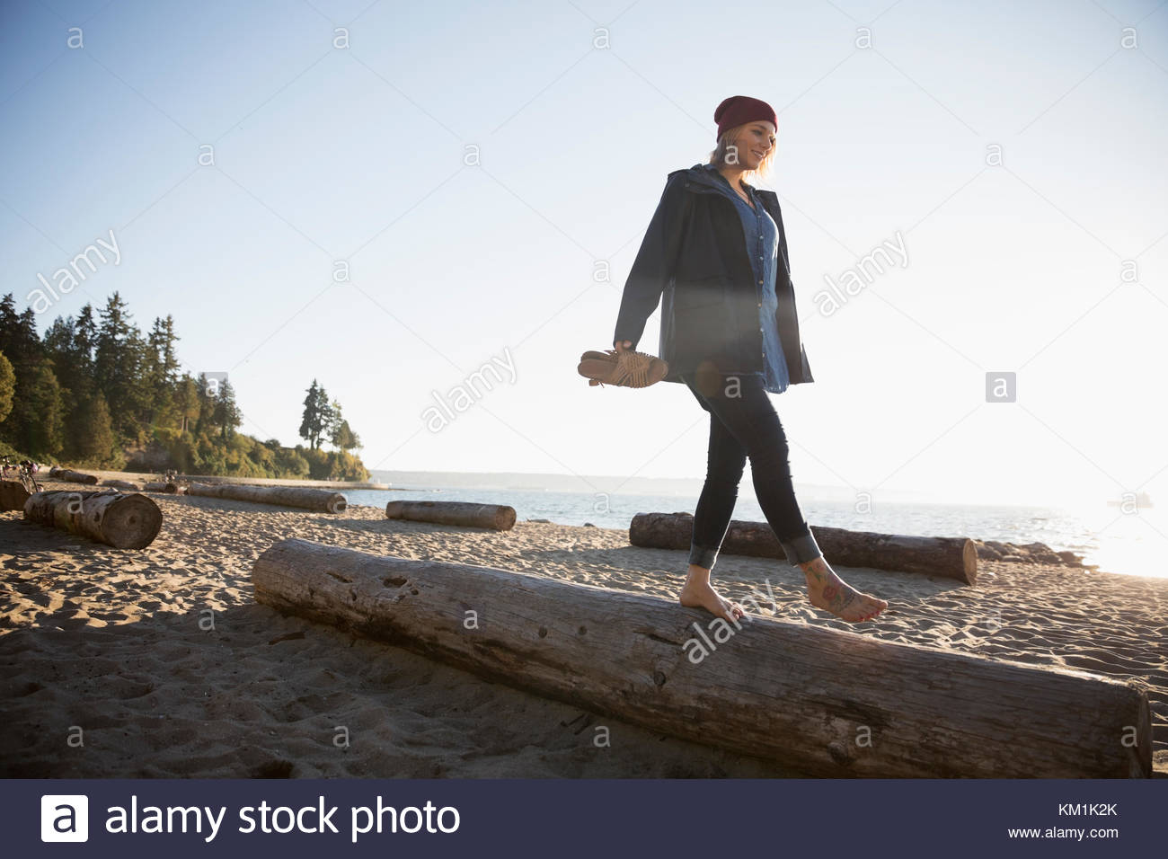 Barefoot woman walking, balancing on log on sunny ocean beach Stock Photo