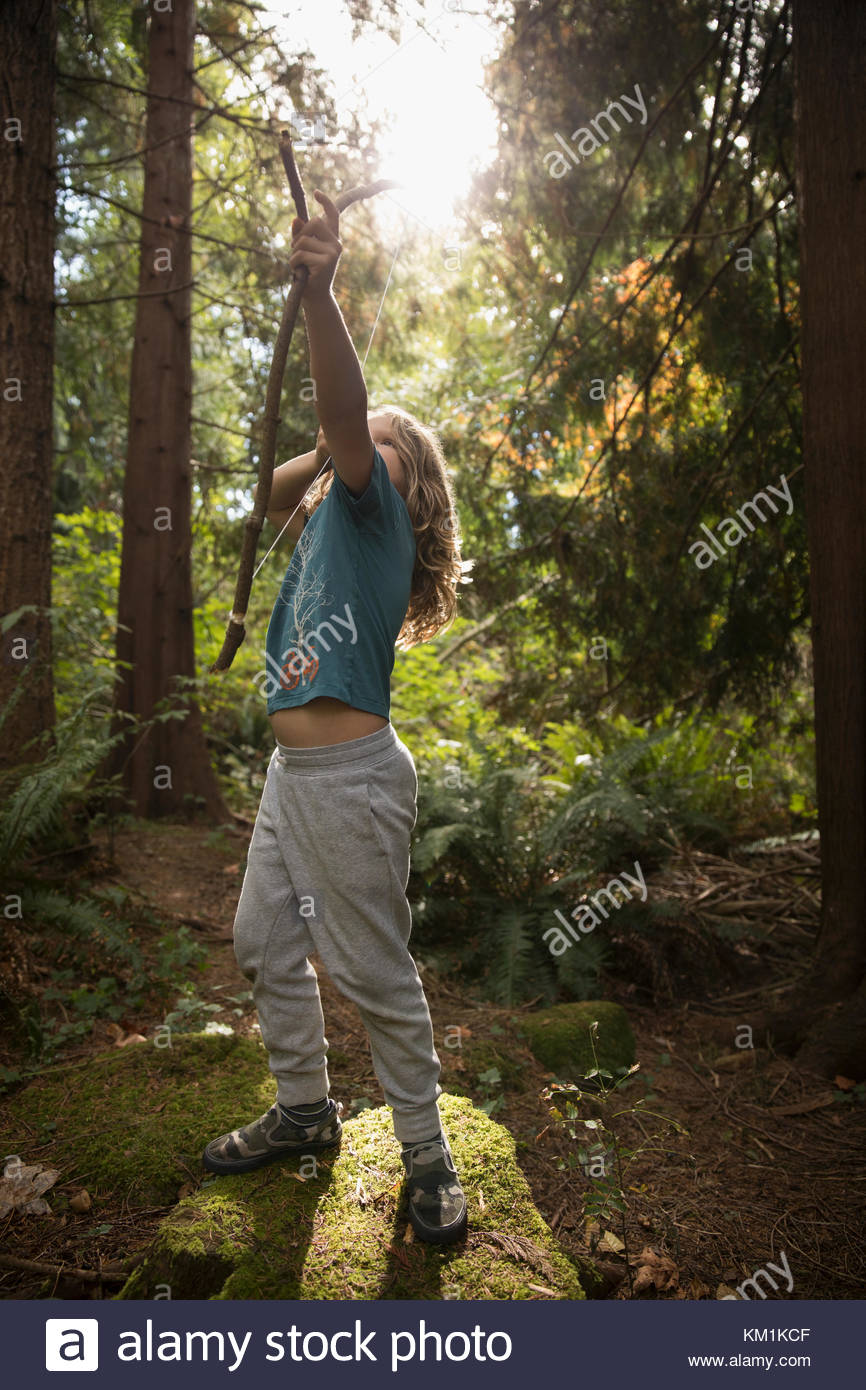 Girl aiming bow and arrow in sunny woods Stock Photo