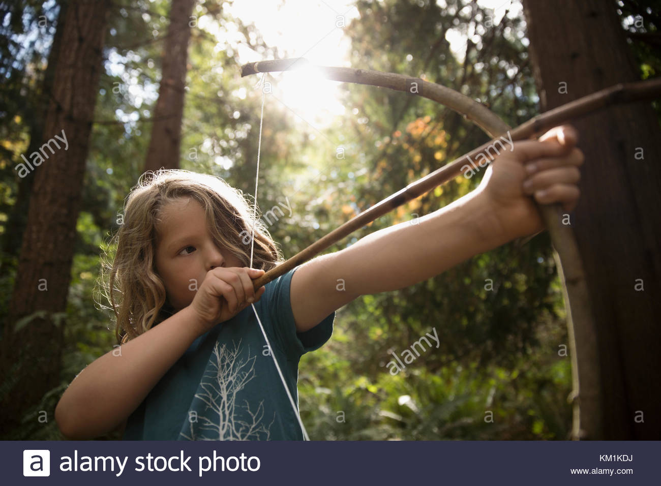 Tough girl aiming bow and arrow in woods Stock Photo