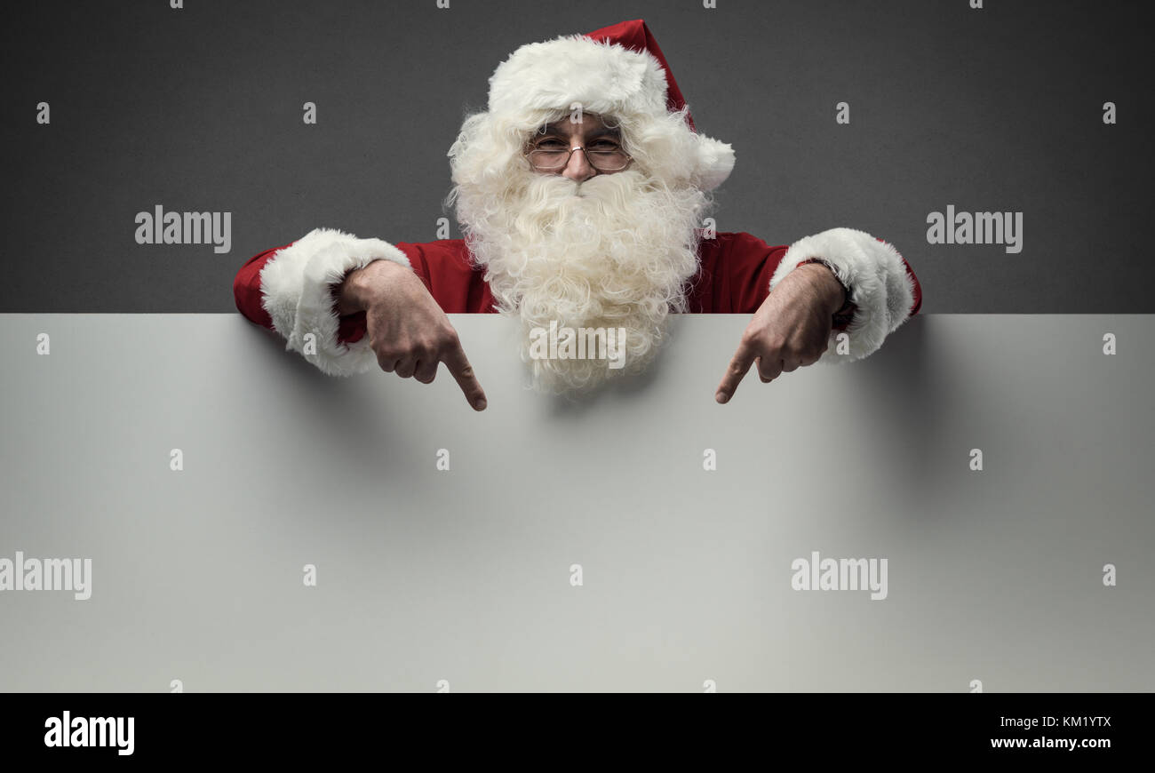 Cheerful Santa Claus pointing at a big blank sign, Christmas and celebrations concept Stock Photo