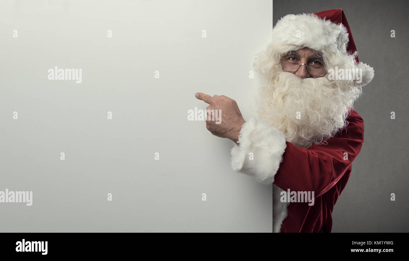 Cheerful Santa Claus pointing at a big blank sign, Christmas and celebrations concept Stock Photo