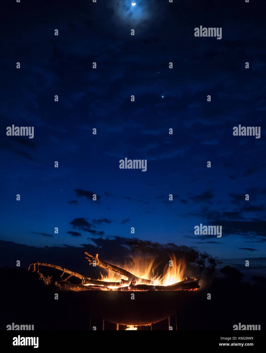 Campfire in the Serengeti, under the moon and a cloudy sky Stock Photo