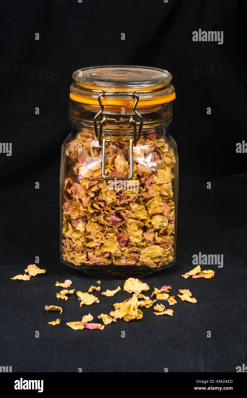 dried rose petals in a glass jar with lid on a black background Stock