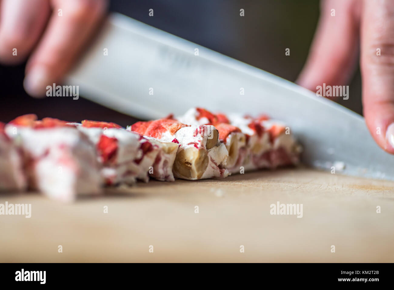 Female Hands Cutting Strawberry Fruit and Nut Nougat with Knife on