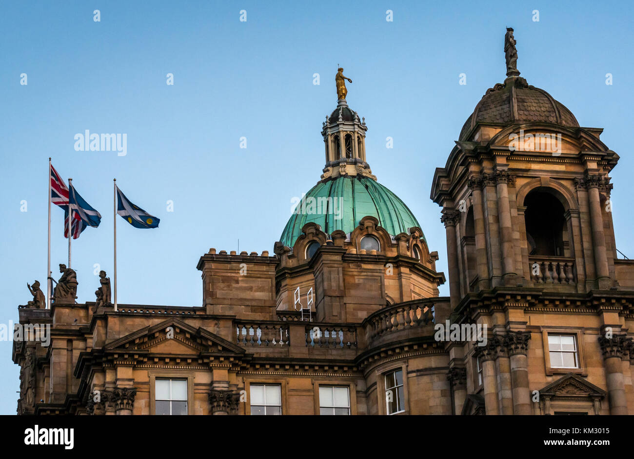Roof of Bank of Scotland headquarters, The Mound, Edinburgh, UK, lit up at dusk with copper dome and flags flying against blue sky Stock Photo