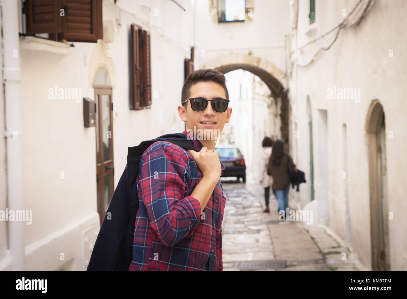 Young handsome italian guy with sunglasses enjoying vacation and posing in a street of the romantic city of Ostuni (Apulia, Italy). Stock Photo