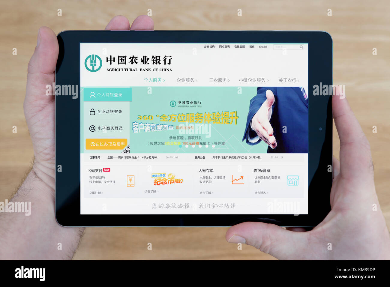 A man looks at the Agricultural Bank of China website on his iPad tablet device, shot against a wooden table top background (Editorial use only) Stock Photo