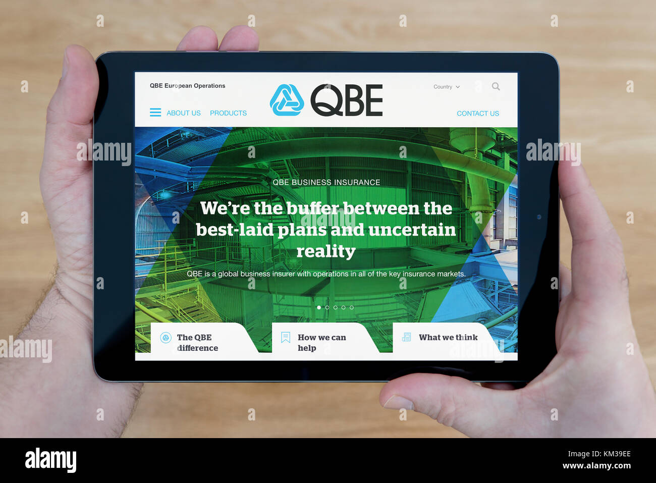 A man looks at the QBE Insurance website on his iPad tablet device, shot against a wooden table top background (Editorial use only) Stock Photo