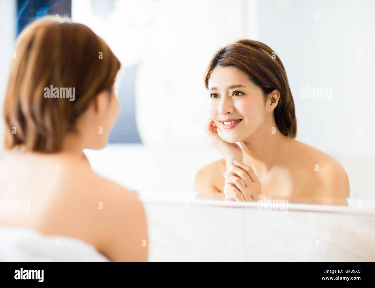 young woman looking on reflection in the mirror at bathroom Stock Photo