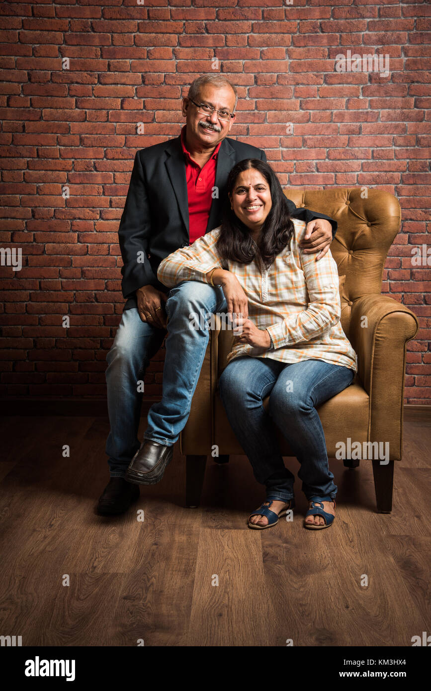portrait of senior indian couple while sitting on sofa of wing chair ...