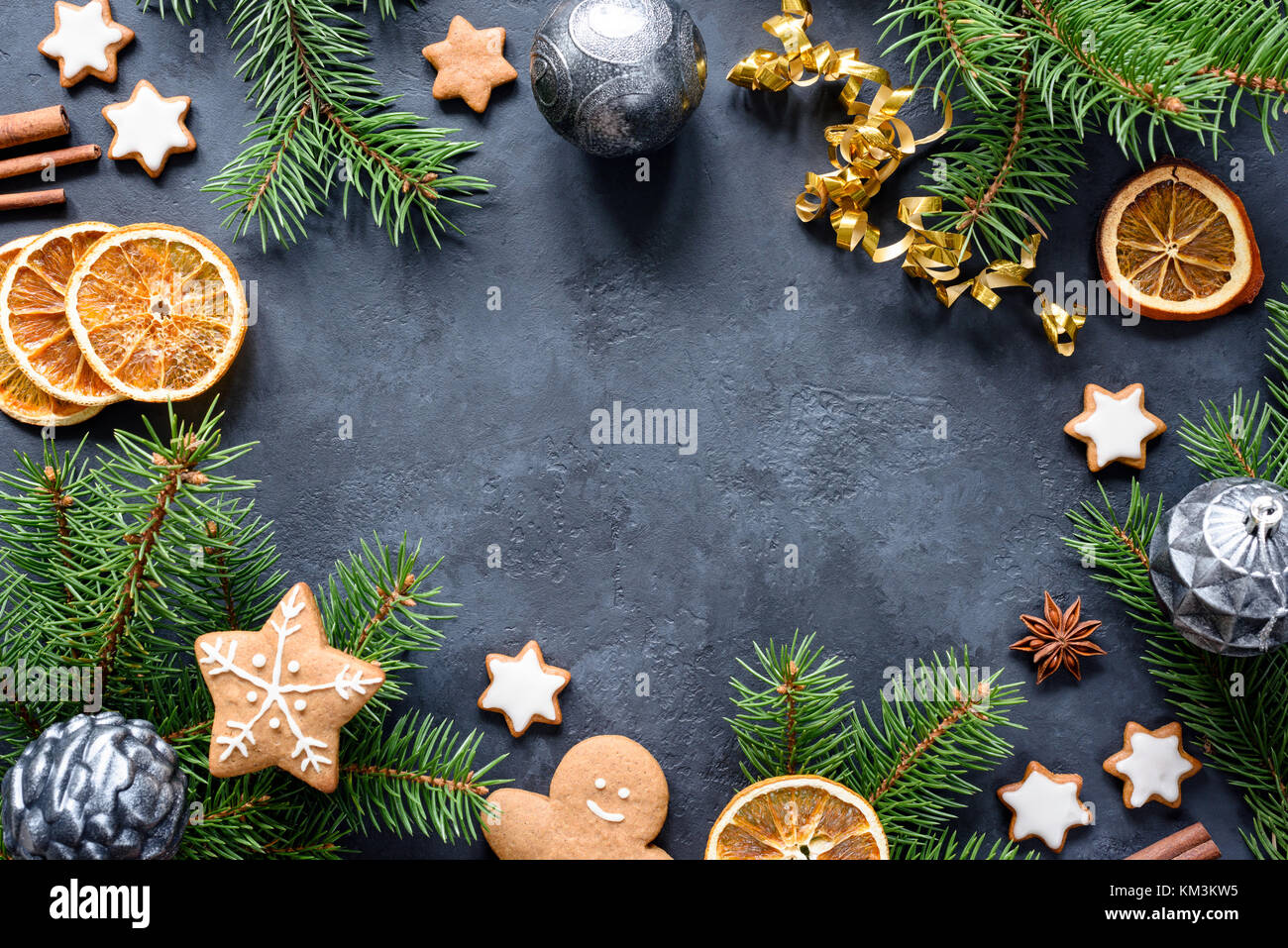 Christmas or New Year frame with fir tree branches, gingerbread cookies, spices, dried orange rings and Christmas toys on stone background. Copy space Stock Photo