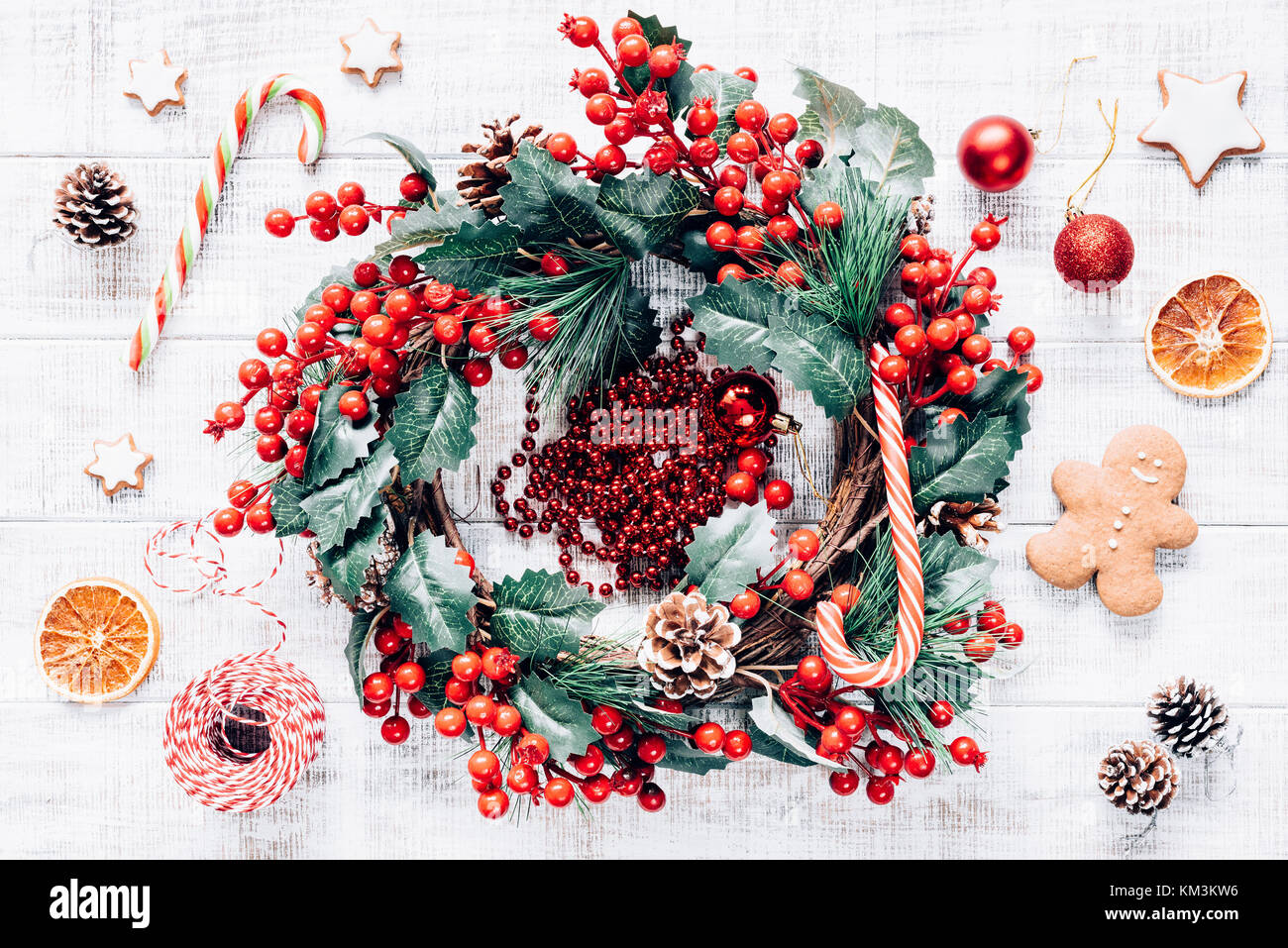 Christmas winter wreath, candy canes, Christmas tree decorations and gingerbread cookies on old white wooden background. Wallpaper, background or holi Stock Photo