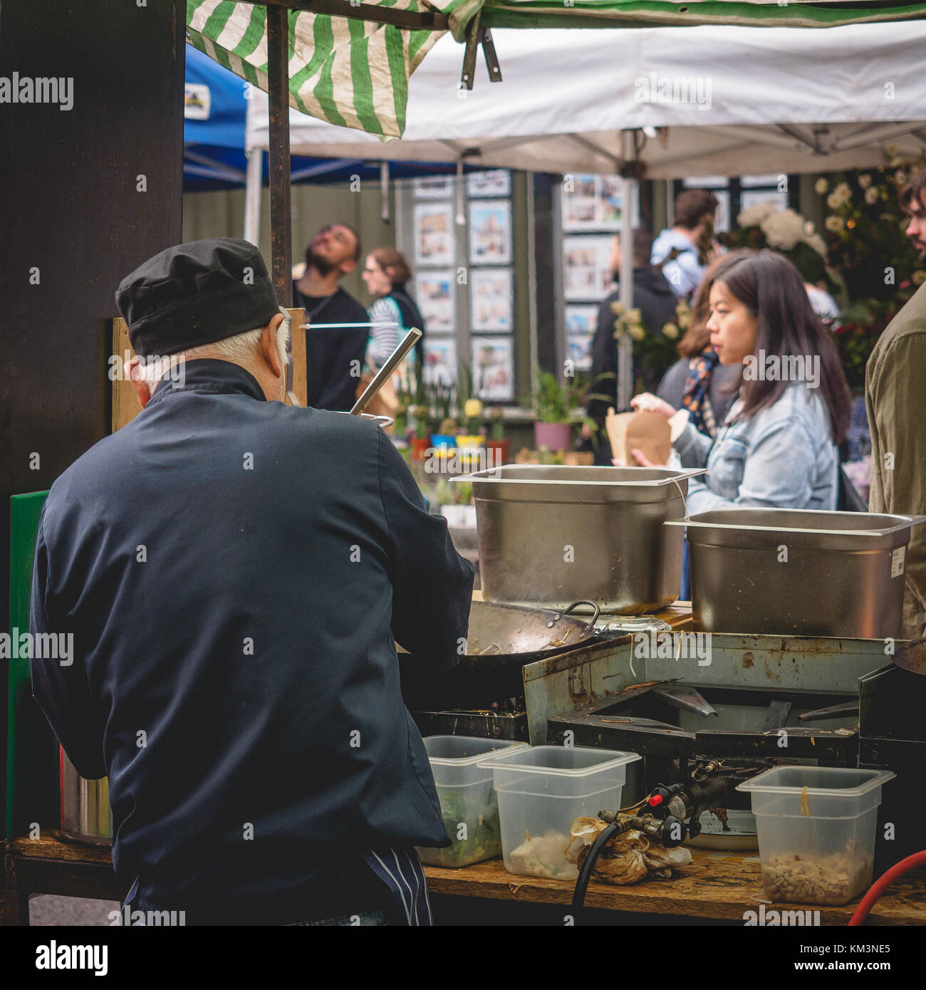 Thai chef preparing food in a street food stall in Broadway Market. East London (UK), August 2017. Square format. Stock Photo