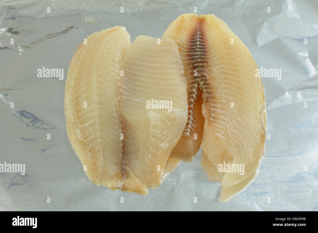 Two fresh raw tilapia fish fillets on aluminum foil to prepare for