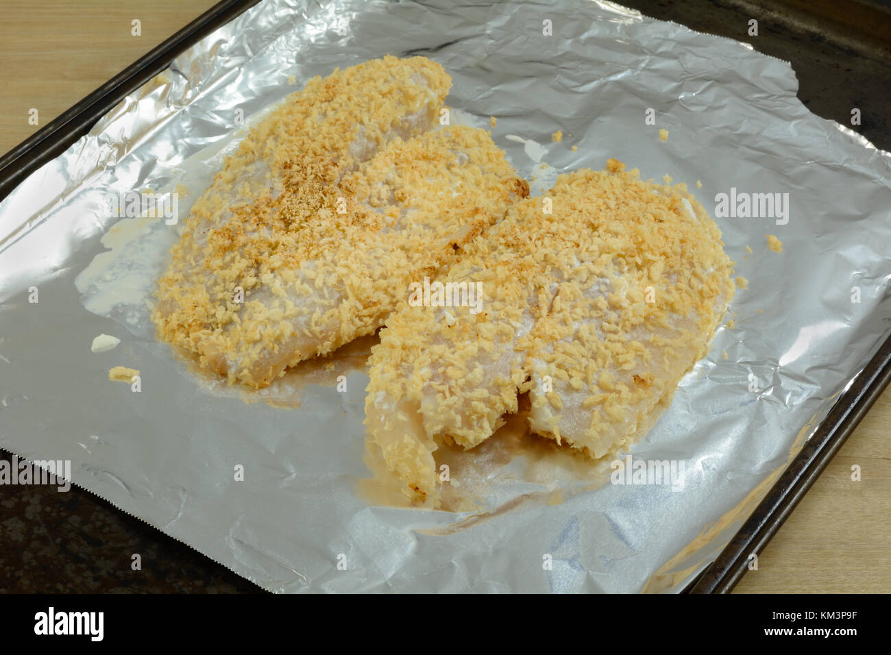 Two raw tilapia fish fillets coated with sour cream and bread crumbs on