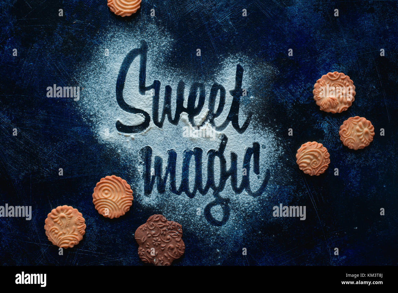 Words Sweet Magic made with flour. Cookies and sugar powder on a dark background. Food typography concept. Sweet flat lay. Stock Photo