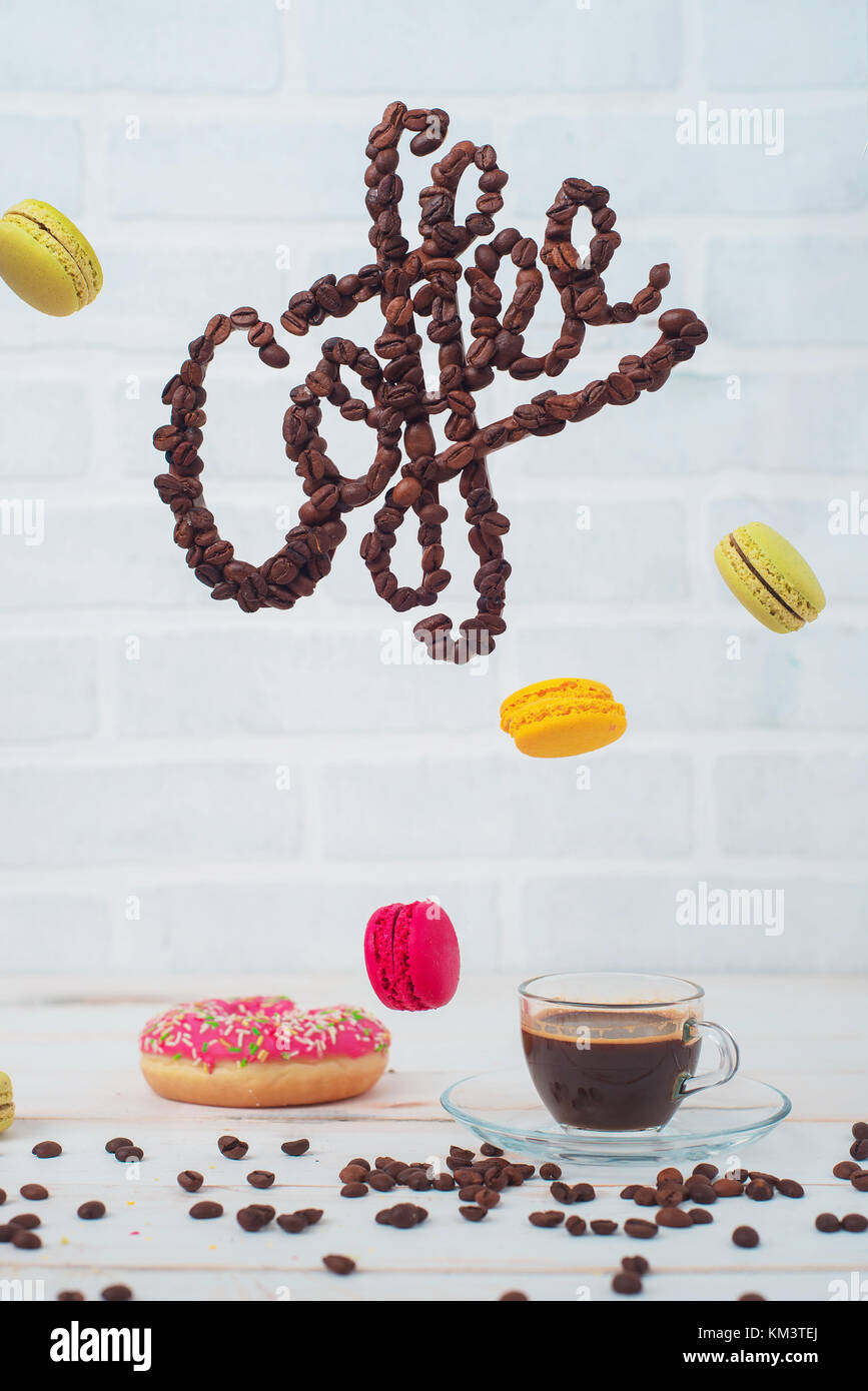 Coffee letters made with beans flying over espresso and macaroons. High key still life with levitation. Stock Photo