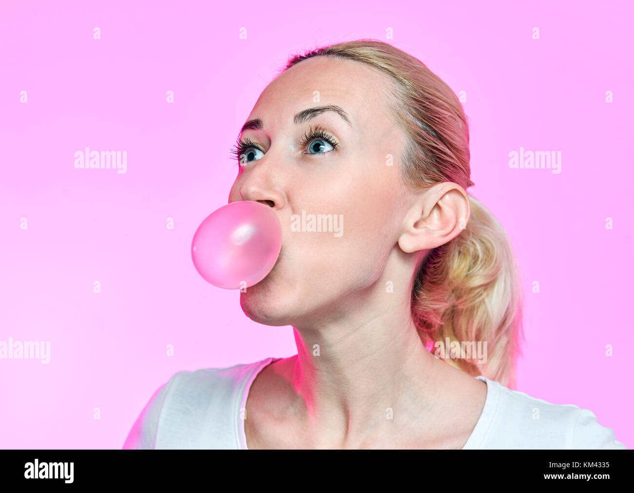 blonde girl inflates a bubble gum on a pink background Stock Photo