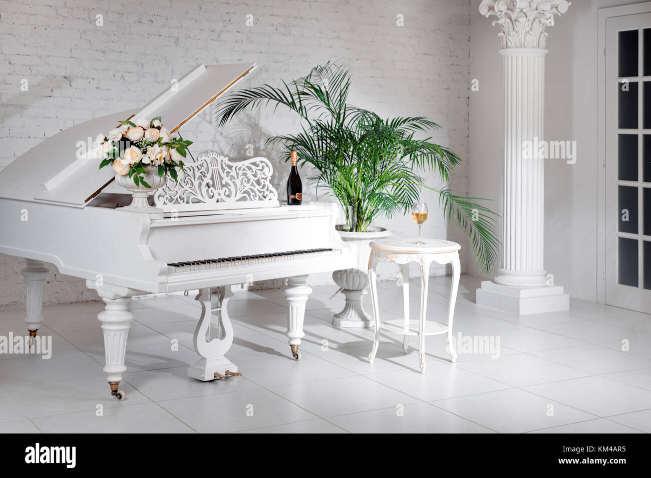 Grand piano in a luxury white classic interior with wine, palms and ...