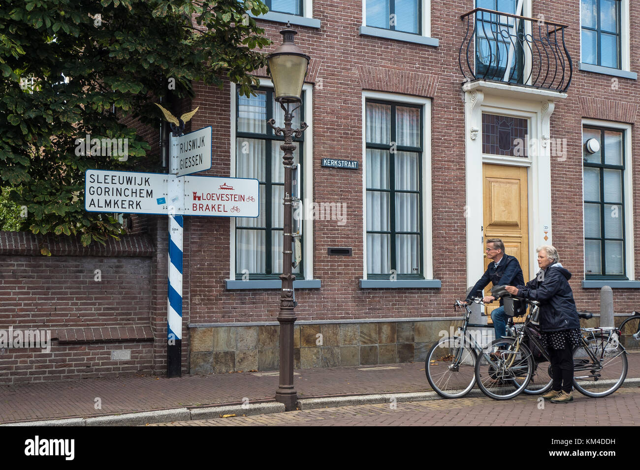 Two tourists on bicycles are pausing in front of an old signpost in Woudrichem, Holland. Stock Photo