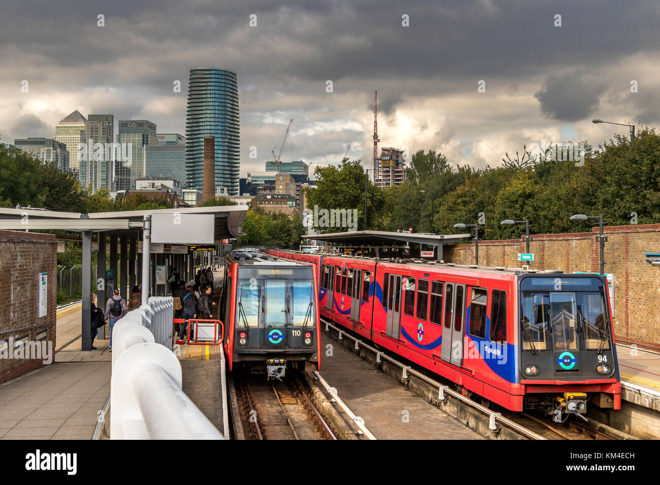 Rail Passengers board a Dockland's Light Railway Train at Mudchute DLR Station with the towers of Canary Wharf in the distance Stock Photo