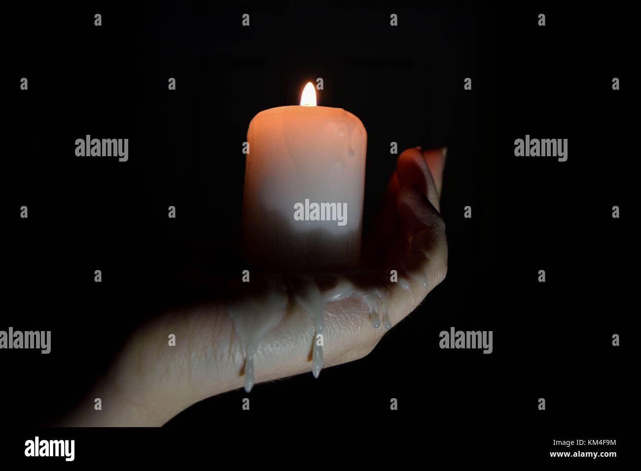 A candle burning, dripping melted max down on to someones hand, in the dark Stock Photo