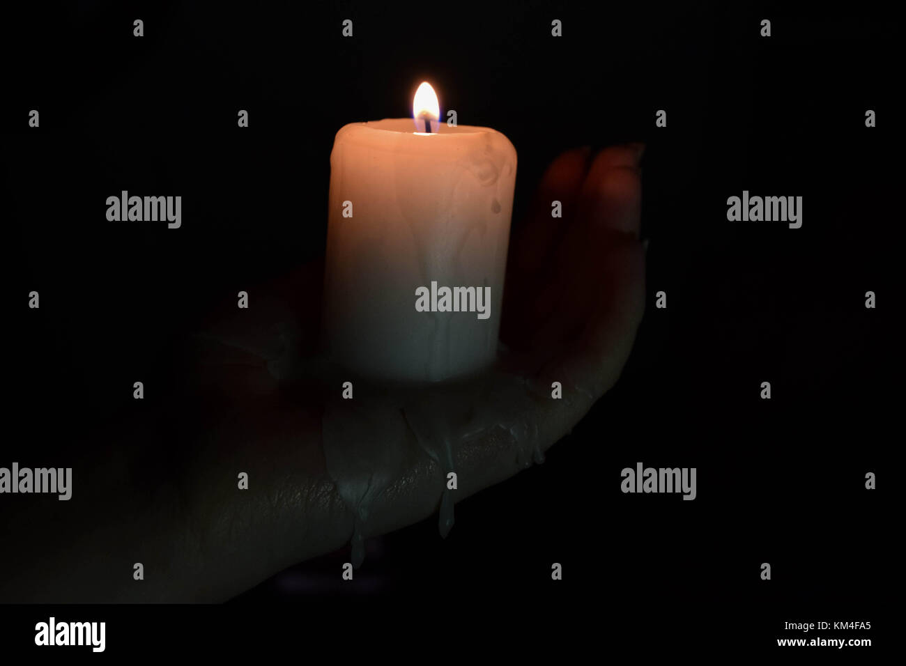 A candle burning, dripping melted max down on to someones hand, in the dark Stock Photo