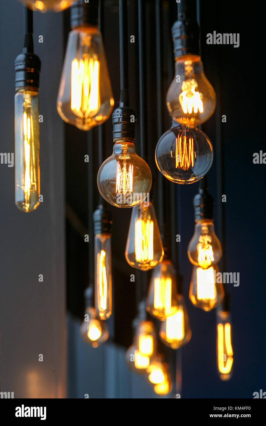 Vintage tungsten filament multiple lamps of different size and style hanging from the ceiling on a black wires as an interior design concept. Energy a Stock Photo