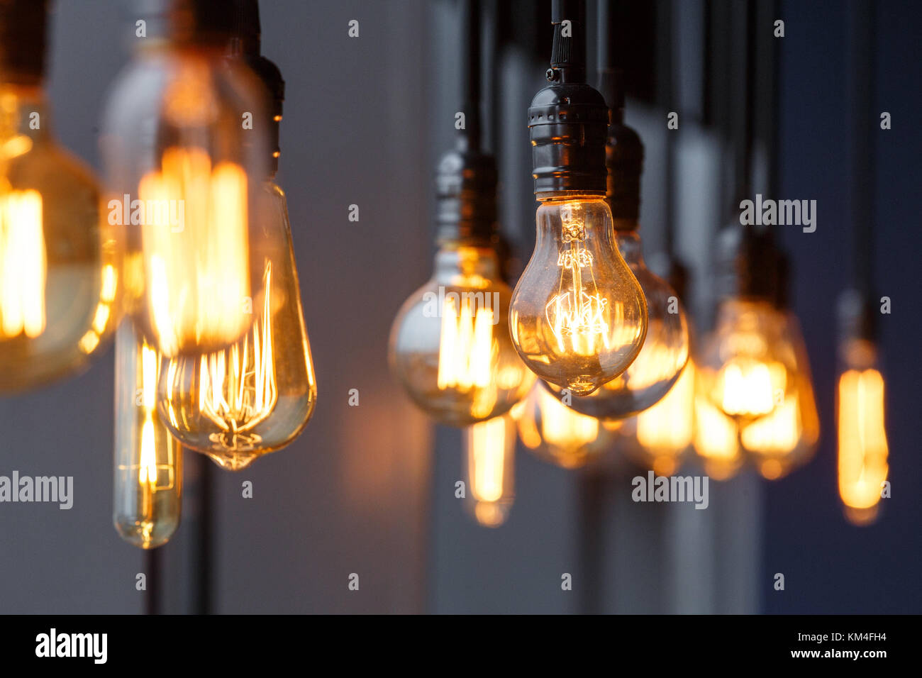 Vintage tungsten filament multiple lamps of different size and style hanging from the ceiling on a black wires as an interior design concept. Energy a Stock Photo