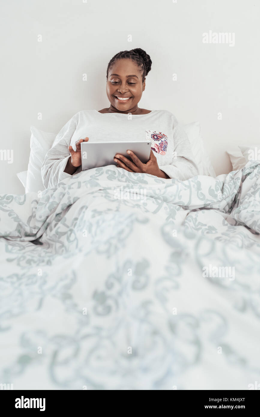 Smiling African woman using a digital tablet in bed Stock Photo - Alamy