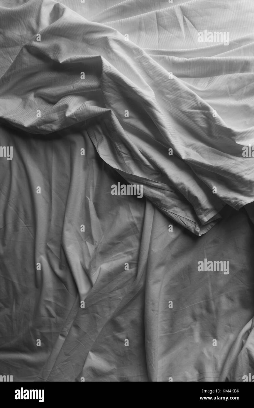 Black and white close up of wrinkled cotton sheets on bed. Stock Photo