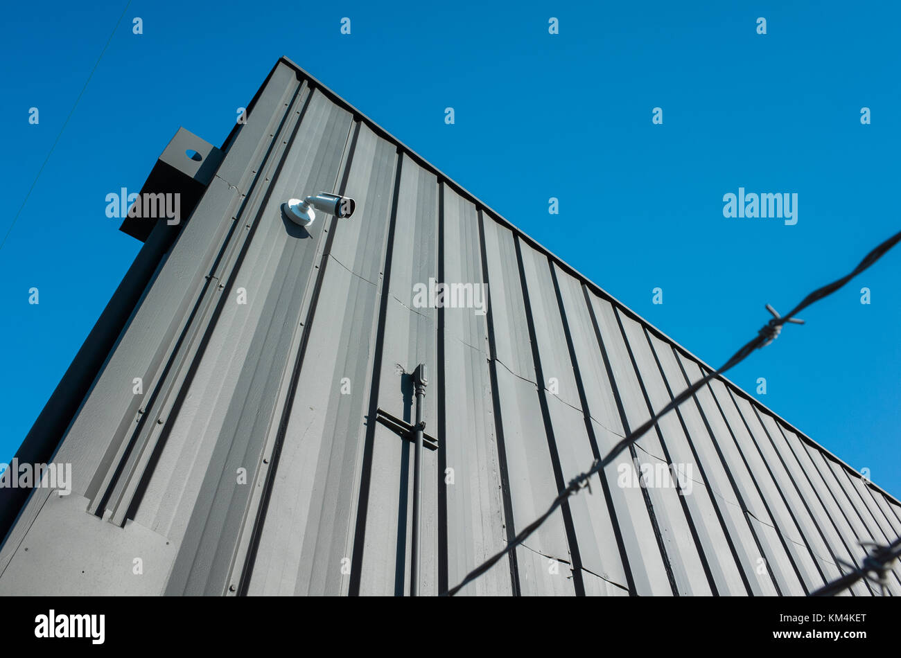 Low angle view of building exterior with surveillance camera, barbed wire in foreground. Stock Photo