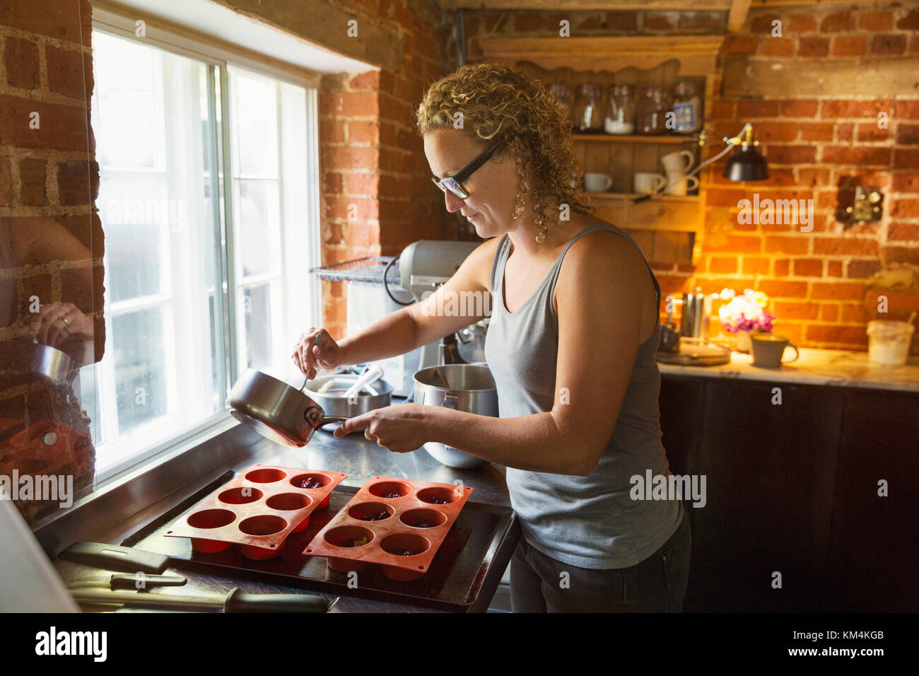 Side view of woman standing in a kitchen, baking, filling silicone molds. Stock Photo