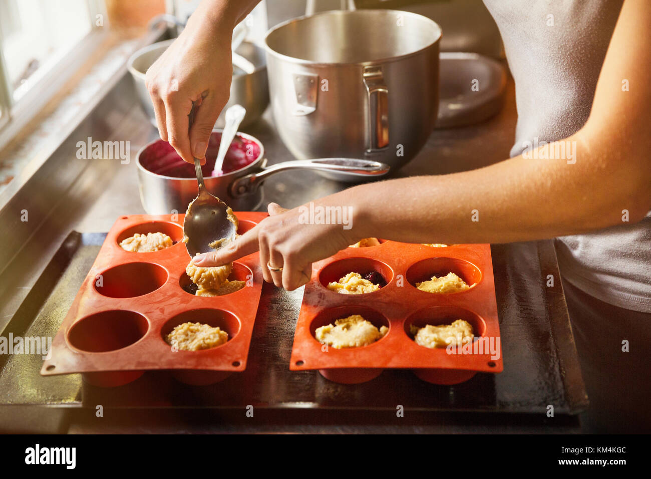 High angle close up person using spoon to place small portions of cake dough into silicone mold. Stock Photo